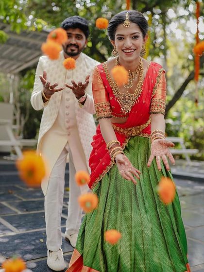 A playful moment during an engagement celebration, with the couple tossing marigold flowers in the air. This captures the fun and festive spirit of the event.