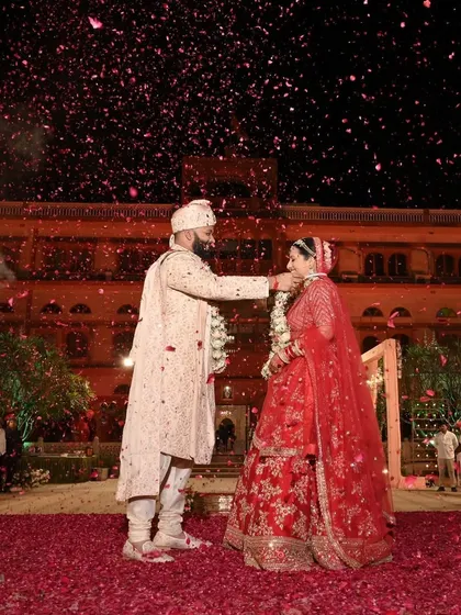 The groom lovingly places the garland around his bride during their royal wedding ceremony, surrounded by a sea of rose petals.