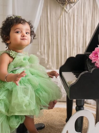 A moment of curiosity during her first birthday shoot. This little one in her green tulle dress explores the miniature piano, a perfect prop for a memorable session.