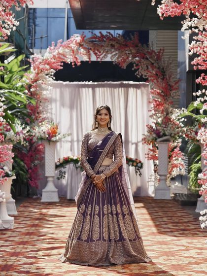 A stunning full-length photo of the mauve-purple lehenga, framed by a beautiful floral arch.