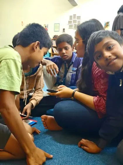 A young boy waves to the camera, surrounded by his friends and a volunteer during a session. These interactions build trust and create a supportive environment where children feel comfortable and happy.