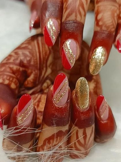 A festive design on henna-adorned hands, featuring red and gold glitter nails with abstract stripes.