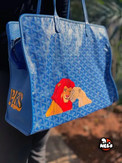 A three-quarter view of the custom Goyard bag, displaying both the main artwork and the side monogram.