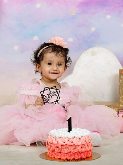 A sweet and simple first birthday setup with a pastel watercolor backdrop. The focus is all on the birthday girl and her delicious ombre cake.