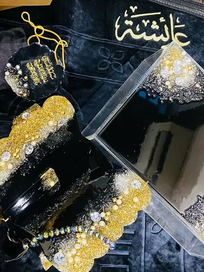 This luxurious black, gold, and silver combo set is a popular choice for a bridal gift. It includes a premium velvet prayer mat, a personalized acrylic Quran box, a resin Quran stand (rehal), a crystal tasbeeh, and a matching car hanging.