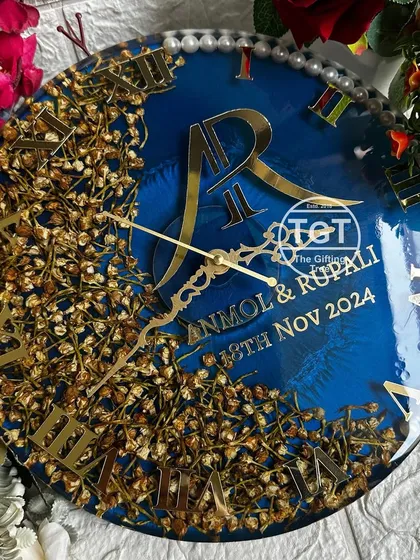 A beautiful 12-inch resin clock preserving a wedding varmala in a full floral arc. The shimmery navy blue base makes the golden monogram and text pop.