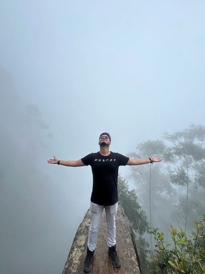 A trekker with arms outstretched at a misty viewpoint in Kodaikanal.