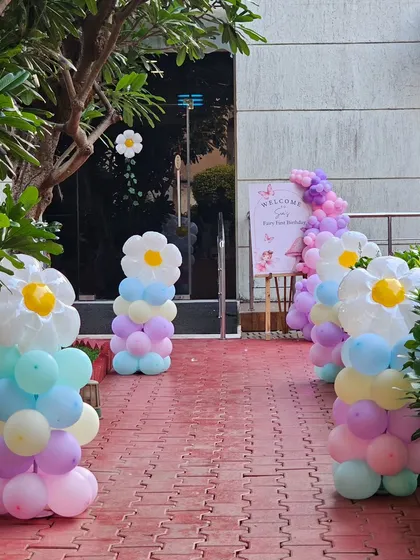 The entrance to the fairy-themed party, lined with balloon columns topped with daisy flowers. A welcome sign greets the guests as they arrive.