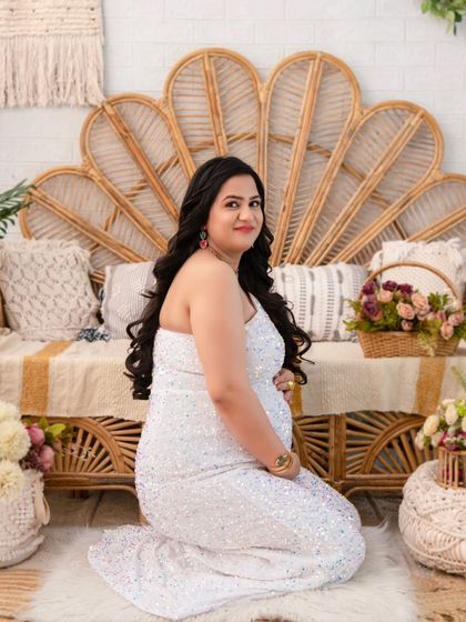 Kneeling gracefully, the mother-to-be smiles warmly in a shimmering white gown. This pose offers a different perspective, emphasizing the fullness of the baby bump and the joy of the moment.
