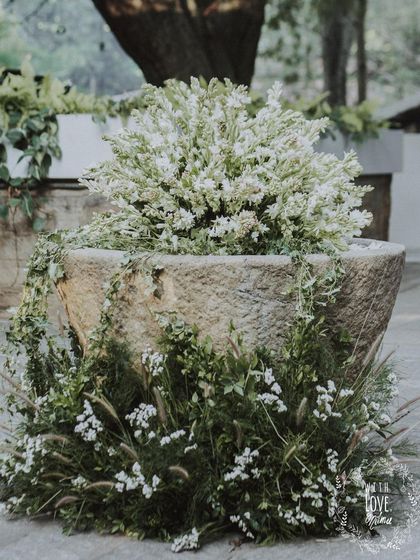 A stone urn overflowing with white flowers and greenery, part of the 'Love in Ruins' wedding decor. The design feels organic and integrated with the venue's architecture.