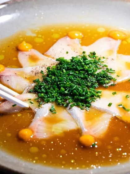 A delicate plate of Hamachi Tiradito. The chopsticks entering the frame add a sense of action and immediacy.