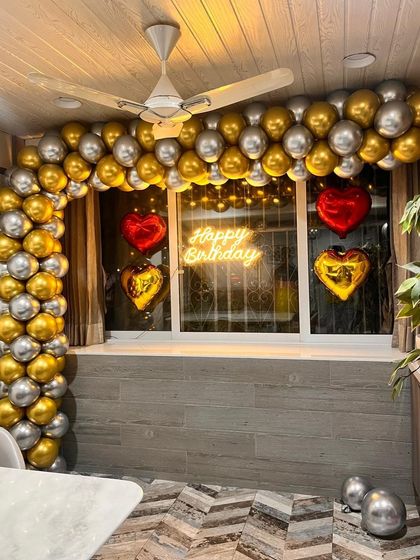 A close-up of the window decoration for the at-home birthday surprise, featuring the glowing neon sign and heart-shaped foil balloons.