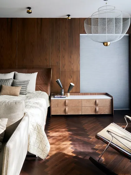 A serene bedroom at the Baid Residence featuring a MOOOI pendant light and a classic rocking chair from B&B Italia. The herringbone wood floor and paneled walls create a warm, enveloping atmosphere.