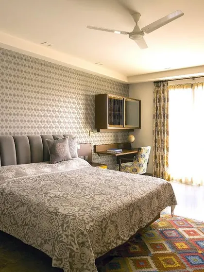The bedroom at Casa K was designed for an avid traveler, balancing practical needs with a dynamic personality. The central bed is framed by a grey headboard and wallpaper, while warm wood tones contrast with a pop of yellow in the custom side table.