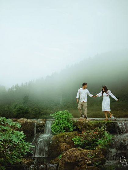 Walking hand in hand across a natural stone bridge, with water cascading below and mist rising from the forest. This adventure-filled shot is perfect for couples who love exploring wild places.