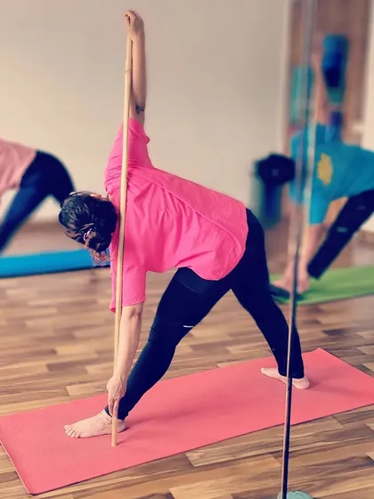Here, a student practices Utthita Trikonasana (Extended Triangle Pose) with a stick. The prop provides feedback for keeping the spine long and the arms in a straight line, enhancing the benefits of the pose.