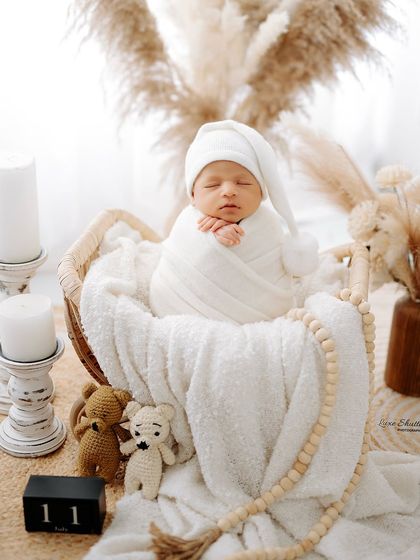 A close-up of the peaceful, all-white setup, focusing on the sleeping baby in a cute pom-pom hat. The soft lighting and neutral tones create a timeless and angelic feel.