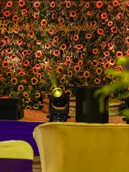 The sunflower wall seen from a distance, with stage lighting in the foreground. This shot shows how the backdrop fits into the larger event space and lighting design.