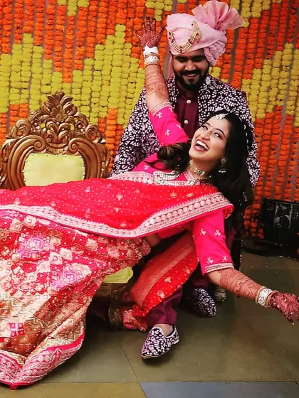 The joy of a wedding day is infectious. This happy couple is celebrating their mehndi ceremony, and you can see the bride's henna-adorned hands as she shares a joyful moment with her partner.