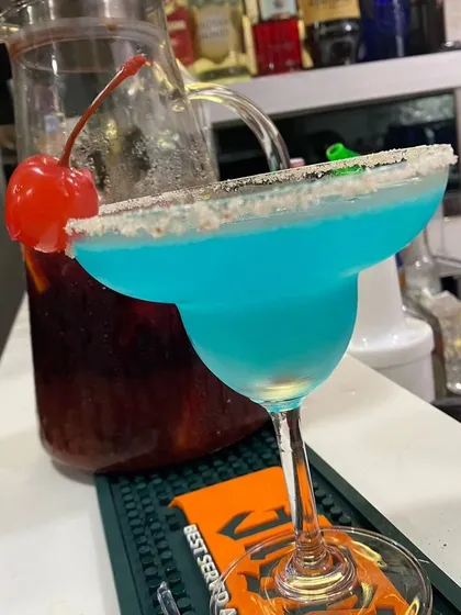 A vibrant Blue Lagoon cocktail, expertly crafted and ready to be served. We pride ourselves on creating visually stunning drinks using premium spirits and fresh ingredients, like this one with a classic sugar-rimmed margarita glass and cherry garnish.