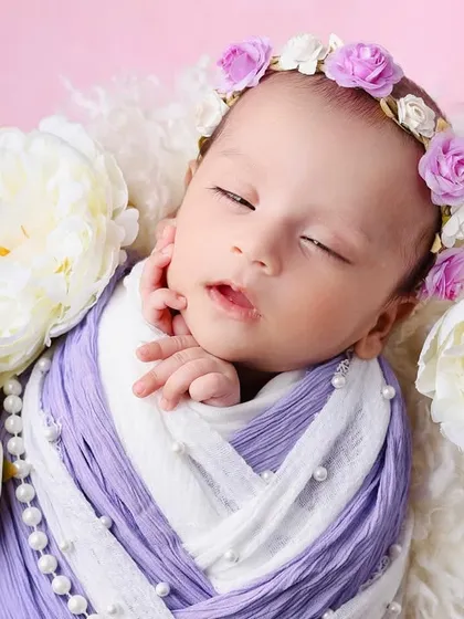 A newborn wearing a purple floral crown, wrapped in a two-tone purple and white swaddle. The large white peonies add a touch of elegance to this portrait.