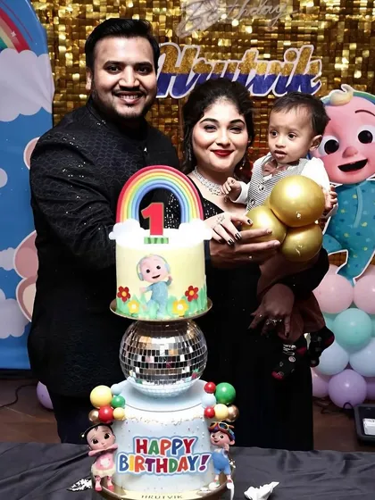 A happy family photo with their son and his colorful Cocomelon first birthday cake.