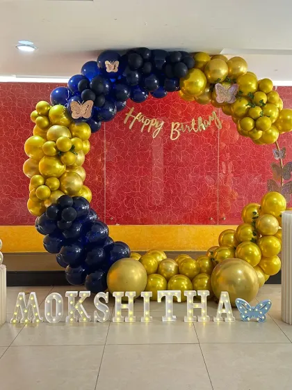 A striking circular balloon arch in navy blue and gold. This bold color combination is perfect for an 18th birthday, with butterfly accents and marquee letters adding a personalized touch.
