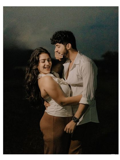 A playful and intimate moment captured in a single frame. His hand covering his mouth in laughter while they embrace shows the fun and comfortable dynamic between the couple.