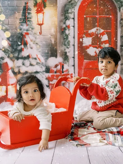 Siblings enjoying the Christmas setup together. The older brother gives his baby sister a ride in the festive red sleigh.