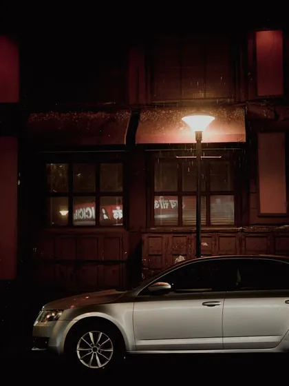 A silver sedan is parked under the warm glow of a streetlight on a rainy Mumbai night. This atmospheric shot captures a quiet, cinematic moment amidst the city's nocturnal ambience.