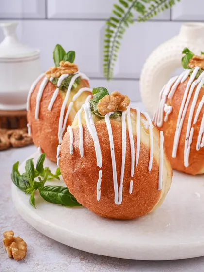 Pesto and walnut bombolonis, an interesting savory twist. The styling with fresh basil and a white chocolate drizzle makes them look intriguing and gourmet.