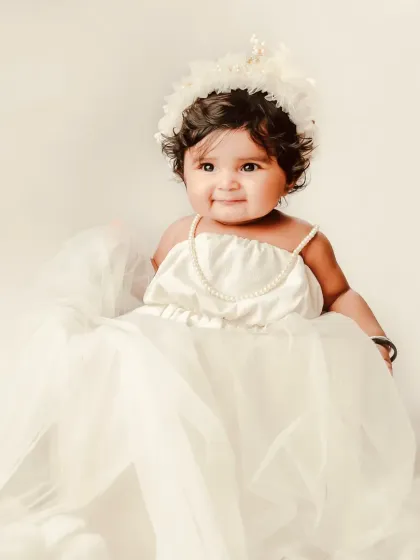 A little angel in a flowing white dress and delicate crown. The soft, ethereal lighting and cloudy backdrop create a truly magical portrait.