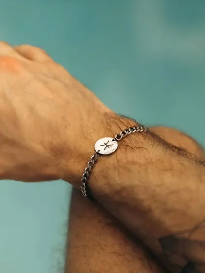 A man wearing my silver chain-link bracelet featuring a custom-engraved disc with the Pisces zodiac symbol. This style offers a modern alternative to the classic cuff.