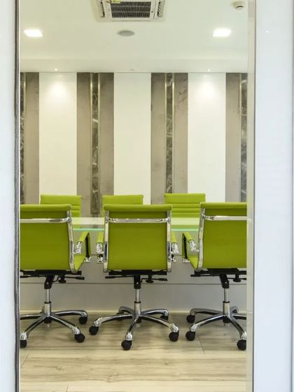 A sleek and modern workspace featuring a minimalist reception desk with a marble accent and a peek into a conference room with vibrant green chairs.