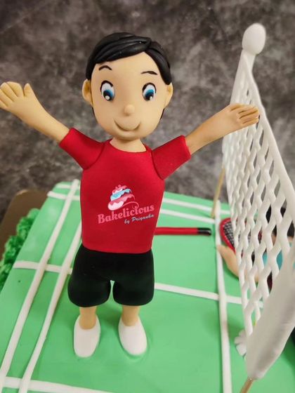 A close-up of the winning player on the badminton cake, complete with a tiny "Bakelicious" logo on his shirt.