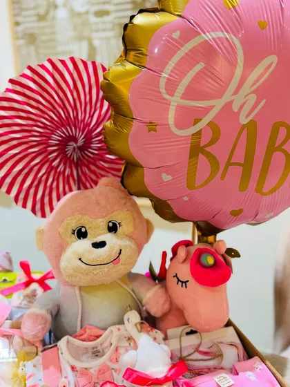 An 'Oh Baby!' balloon crowns this adorable hamper, which includes a cuddly monkey, a unicorn toy, and beautifully wrapped newborn clothes.
