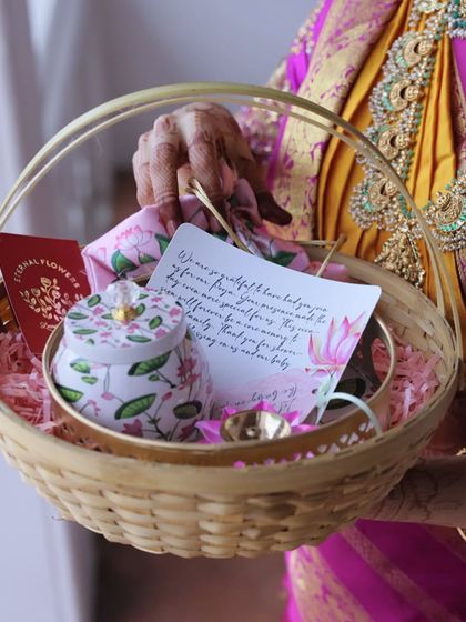 A detailed view of the 'Valakappu' return gift basket, showing the personalized note and floral-patterned items inside, held by the mother-to-be in her beautiful saree.