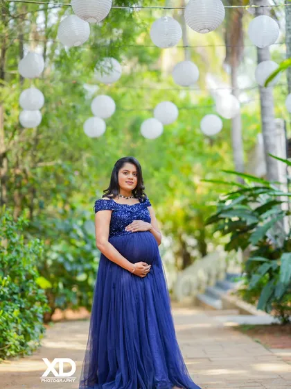 A graceful solo portrait of the mother-to-be in a deep blue gown, surrounded by hanging white lanterns.