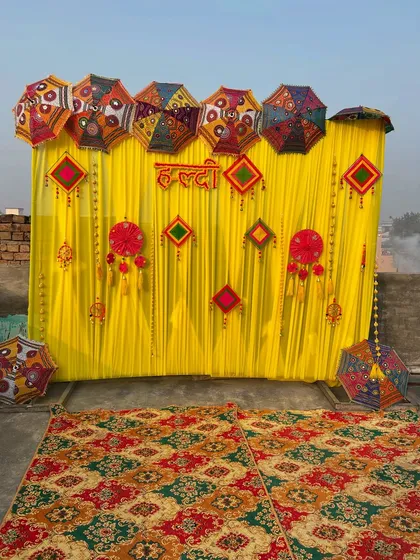 A vibrant and traditional Haldi backdrop for an outdoor space. We used bright yellow drapes as the base and layered them with colorful phulkari umbrellas and decorative hangings to create a rich, textured look that is perfect for photos.