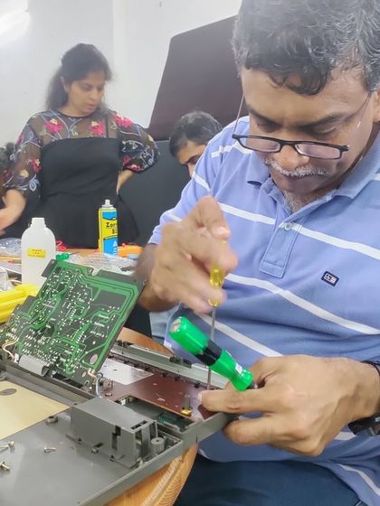 A mentor carefully works on a circuit board from an electronic device. These sessions offer a deep dive into how our gadgets function and how they can be repaired.
