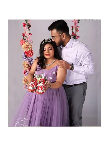 Holding tiny shoes, a sweet symbol of the little one to come. This couple shares a tender moment on the floral swing, dreaming of their future.
