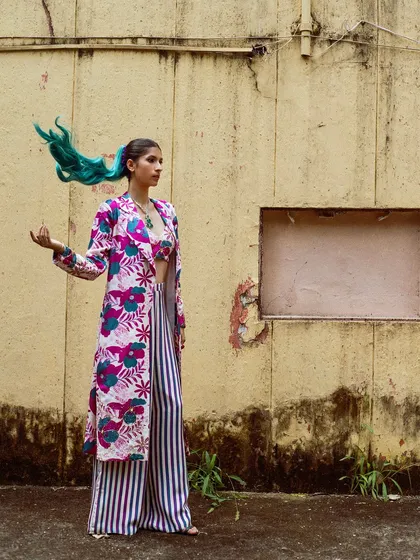 A full-length shot that captures the movement of the model's teal-colored hair and the flowy jacket. This image is dynamic and full of personality.