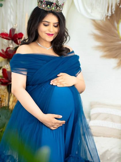 A serene portrait of an expecting mother in a deep blue tulle gown. Her gentle hold on her baby bump and the soft studio lighting create a feeling of peace and anticipation.