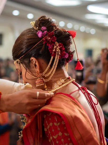 A candid shot from a wedding ceremony, focusing on the intricate bridal hairstyle with floral details and traditional jewellery.