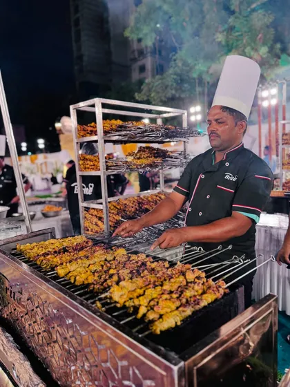 A chef at the grill, managing multiple skewers of Chicken Zafrani Tikka, ensuring each piece is perfectly cooked.