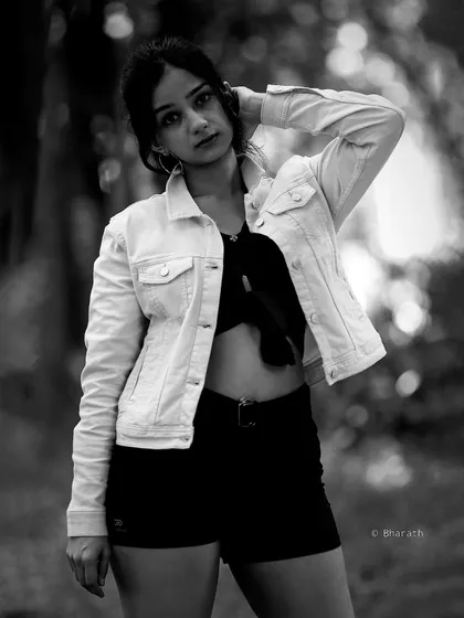 A three-quarter monochrome portrait with a confident pose. The out-of-focus natural background creates a beautiful bokeh effect.