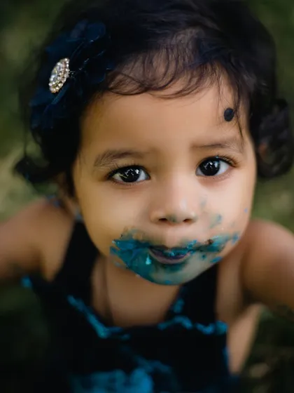 A joyful and messy close-up of a one-year-old's face, delightfully covered in blue cake frosting during her first birthday cake smash. This captures the pure, uninhibited fun of celebrating childhood milestones.
