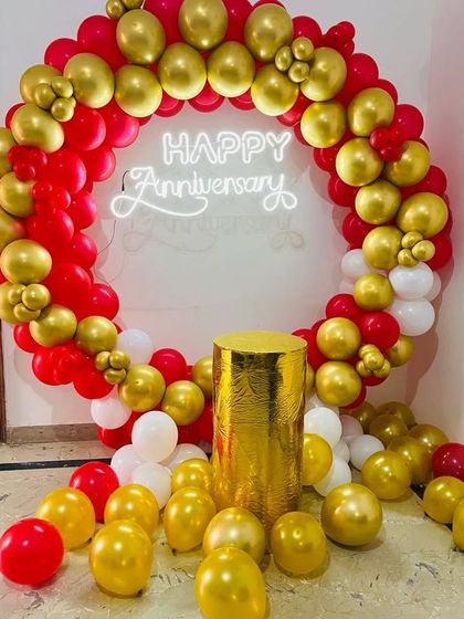 A classic and bold anniversary backdrop. I used a circular arch of red, gold, and white balloons with a 'Happy Anniversary' neon sign and a golden pedestal for the cake.