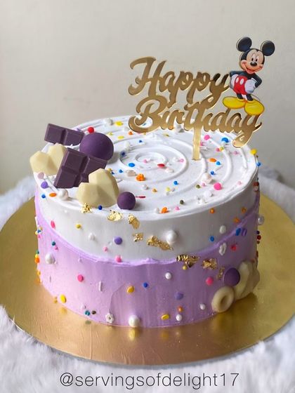 A playful Mickey Mouse birthday cake with a fun purple and white design. The colorful sprinkles and chocolate accents add to the celebration.