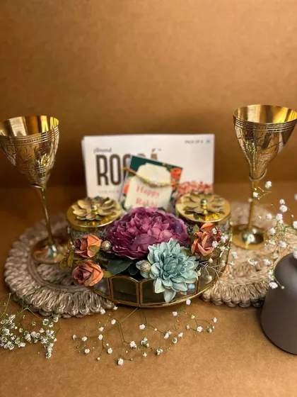 A Royal Rakhi Affair. This vintage-themed hamper for Rakshabandhan features elegant brass wine goblets, a floral centerpiece, and a 'Happy Rakhi' card to celebrate the special bond.